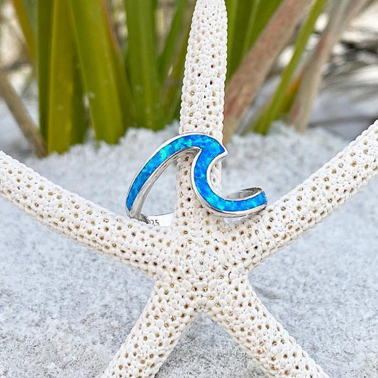 Silberner Wellenring mit blauem Opal auf Seestern im Sand, maritimer Schmuck, Strandaccessoire.