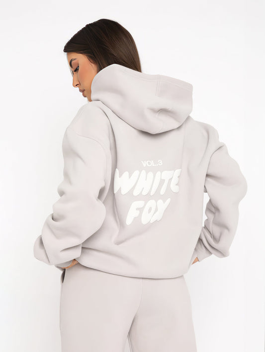 Frau in grauem Hoodie mit "White Fox" Aufdruck, Kapuze, lässiger Stil, Streetwear-Mode.