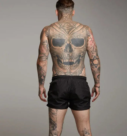 Mann mit großem Totenkopf-Tattoo auf dem Rücken, trägt schwarze Shorts.