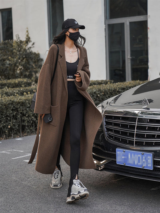 Frau in braunem Trenchcoat, schwarze Leggings, Sneaker, neben Auto, modisch, urbaner Stil.