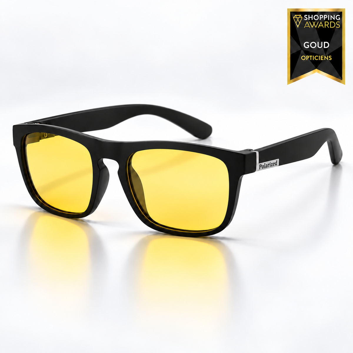 Nachtfahrbrille mit mattschwarzem, eckigem Rahmen und gelben Gläsern, schräg von vorn auf hellem, spiegelndem Untergrund. 9