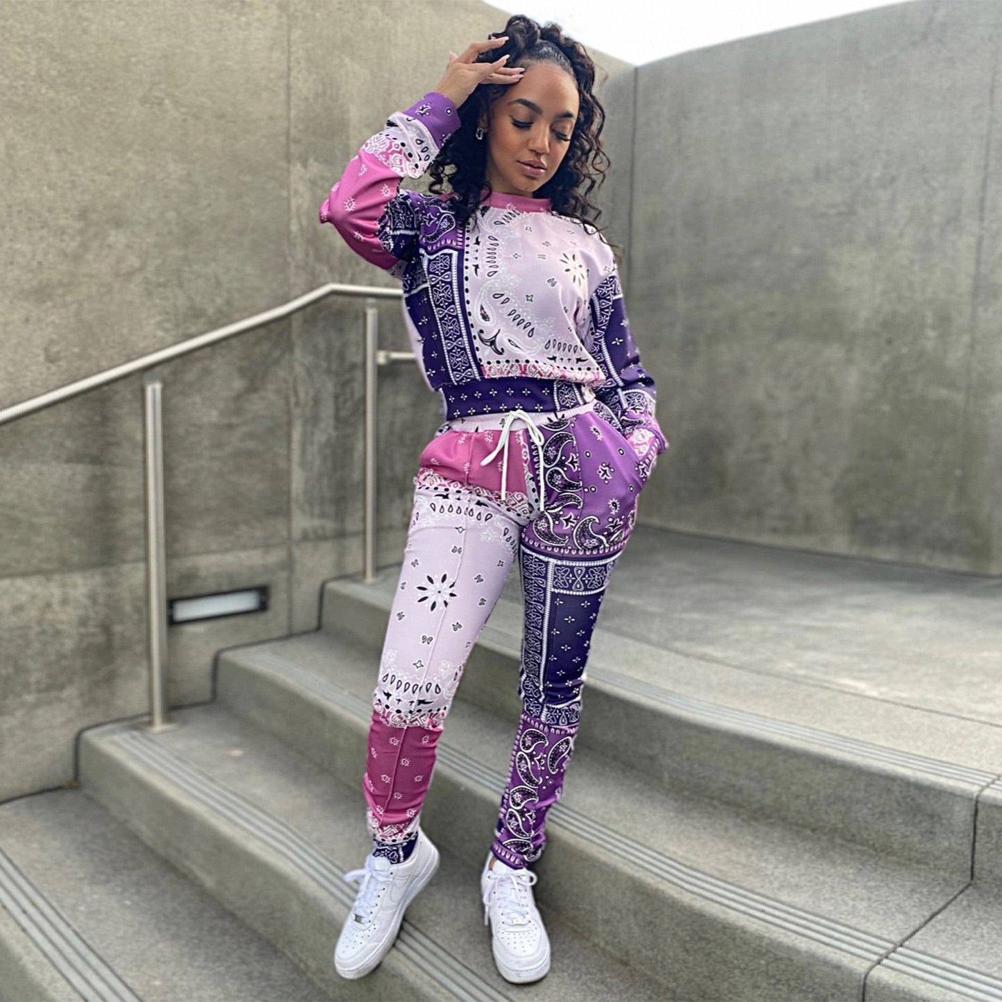 Frau in lila-rosa Bandana-Print Jogginganzug auf Treppe, modisch, urbaner Stil.