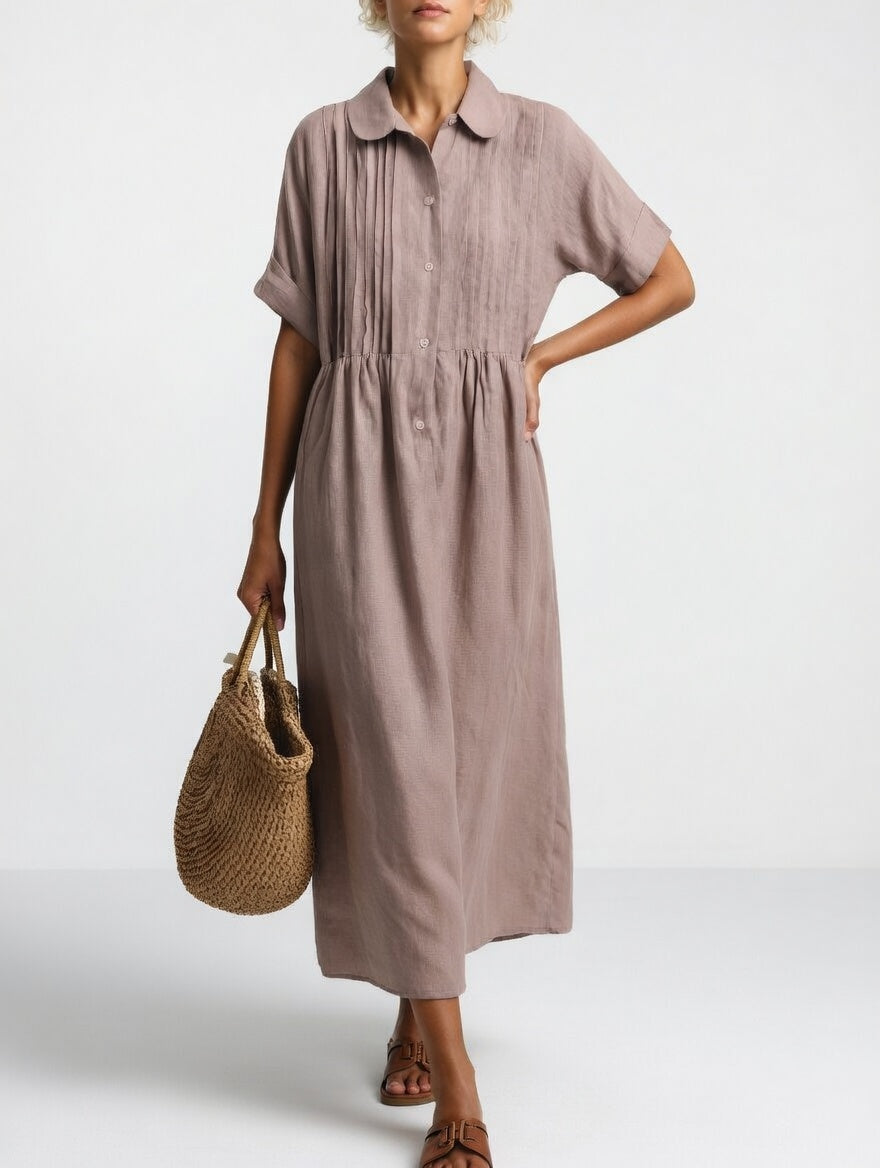 Maxikleid in gedecktem Mauve mit Biesen am Oberteil, Knopfleiste und Kurzärmeln, Hand in der Hüfte, Korbtasche in der Hand. 8
