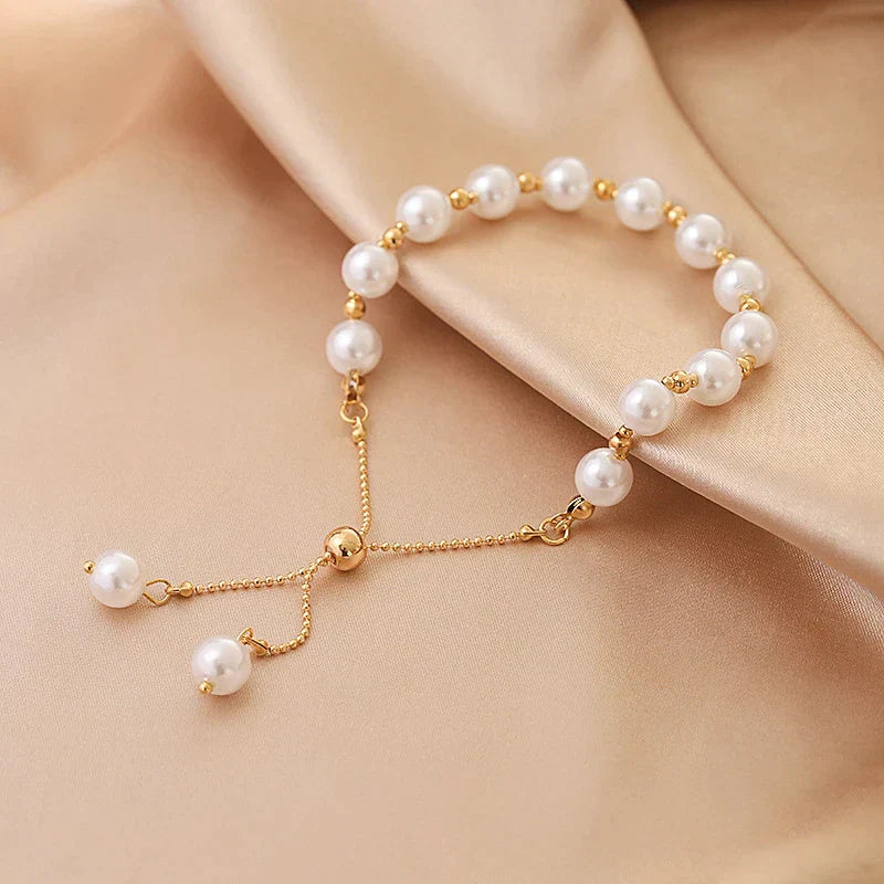 Goldenes Armband mit weißen Perlen auf beigem Stoff, eleganter Schmuck, Damenaccessoire.