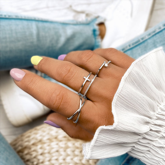 Damenhand mit silbernen Ringen, Kreuzdesign, pastellfarbene Nägel, weiße Bluse, Jeans.
