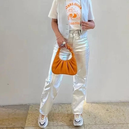 Frau mit orangefarbener Handtasche, silberner Hose, weißem T-Shirt und Sneakers.