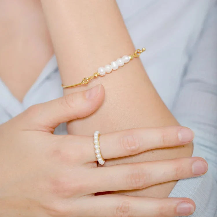 Goldenes Armband und Ring mit weißen Perlen auf Handgelenk, eleganter Schmuck für Damen.