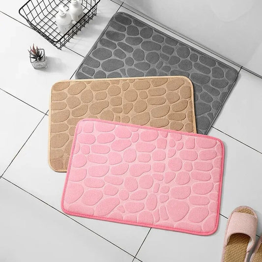 Drei Badematten in Grau, Beige und Rosa mit Steinmuster auf Badezimmerboden.