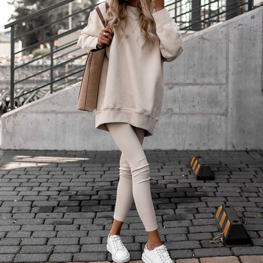 Frau in beigem Oversize-Pullover und Leggings, weiße Sneaker, beige Tasche, urbaner Hintergrund.