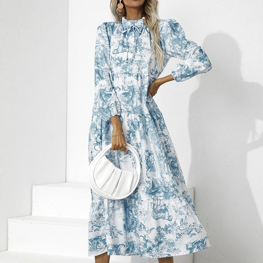 Frau in blau-weißem Maxikleid mit Muster, hält weiße Handtasche, elegante Mode.