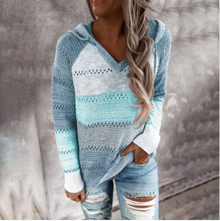 Frau in blauem Strickpullover mit Kapuze und zerrissenen Jeans vor grauem Hintergrund.