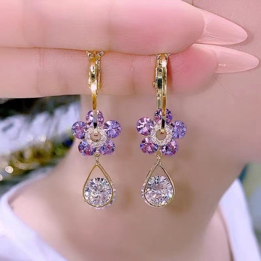 Goldene Ohrringe mit lila Blumen und tropfenförmigen Kristallen, eleganter Schmuck.