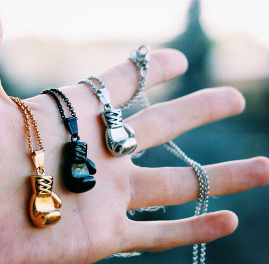 Drei Boxhandschuh-Halsketten in Gold, Schwarz und Silber auf Hand präsentiert.