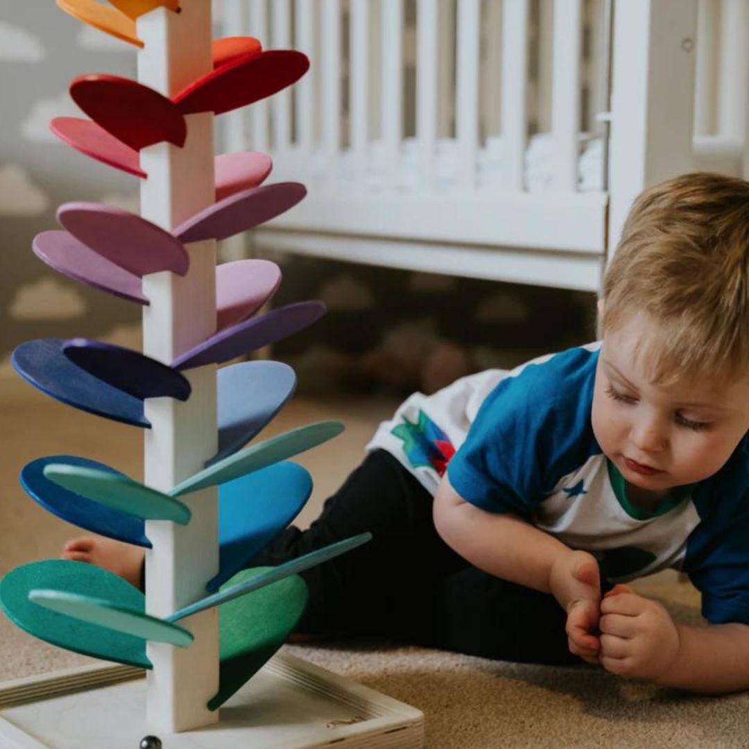 Kleinkind spielt mit buntem Holz-Murmelbaum im Kinderzimmer, Montessori-Spielzeug.