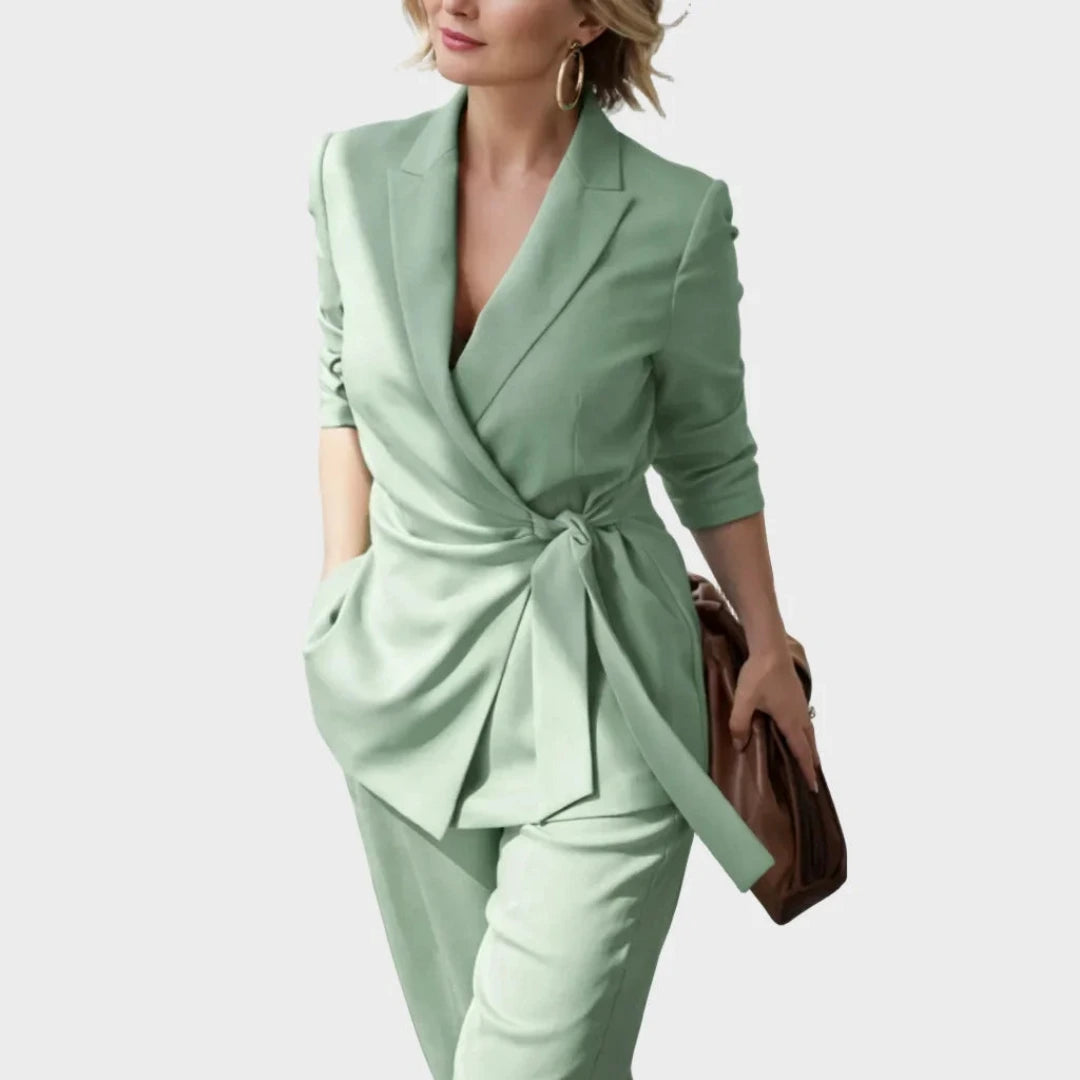 Mintgrünes Set an einer lächelnden Frau mit Creolen und brauner Clutch, Blazer mit geknotetem Gürtel seitlich an der Taille. 6