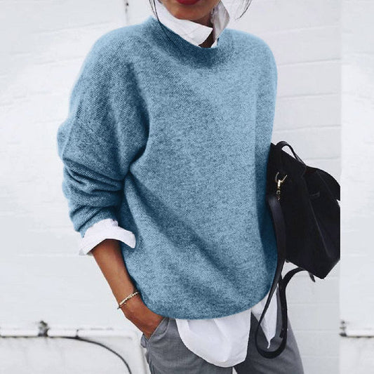 Frau in blauem Strickpullover, weißem Hemd, grauer Hose, hält schwarze Tasche, lässiger Stil.