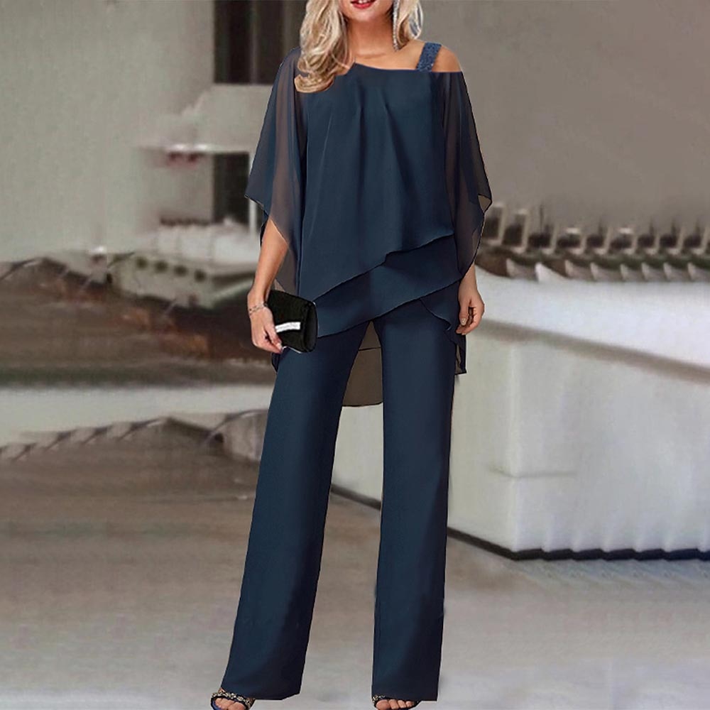 Frau in dunkelblauem Chiffon-Zweiteiler, schulterfrei, elegant, mit schwarzer Clutch.