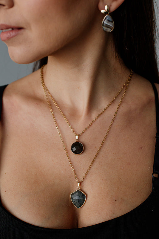 Frau mit goldener Halskette und Ohrringen, schwarzer Anhänger, eleganter Schmuck, Nahaufnahme.