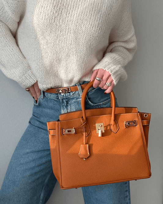 Frau mit brauner Lederhandtasche, Strickpullover und Jeans, modisches Accessoire.