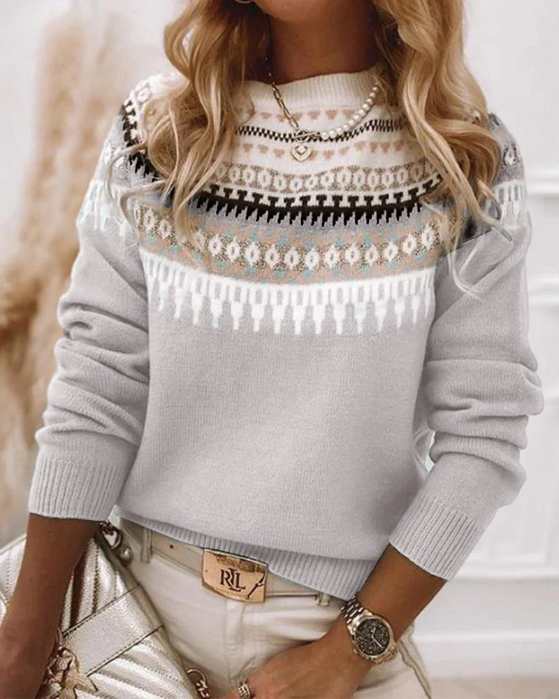 Frau in grauem Strickpullover mit Norwegermuster, goldene Uhr, beige Hose, modisch.