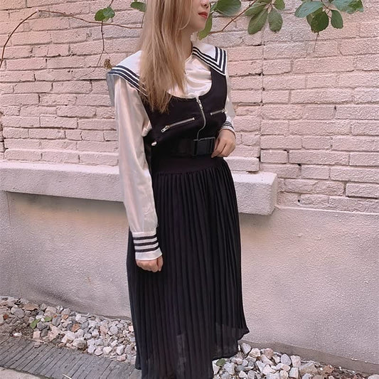 Frau in schwarz-weißem Schulmädchen-Outfit mit Faltenrock vor Ziegelwand.