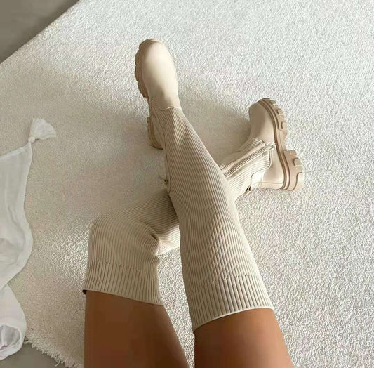 Beige kniehohe Stiefel mit gerippter Struktur auf weißem Teppich, modisch und elegant.