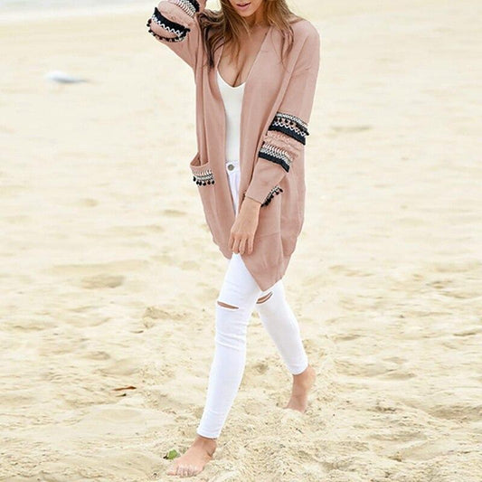 Frau am Strand in rosa Strickjacke mit Stickerei, weiße Jeans, lässige Mode.