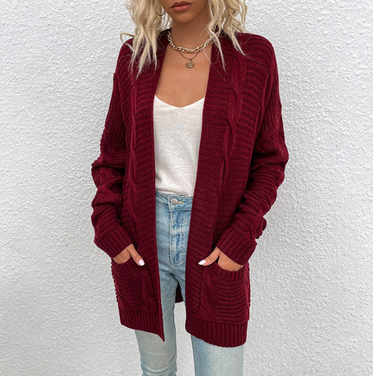 Frau in roter Strickjacke, weißem Top und blauer Jeans vor weißer Wand.