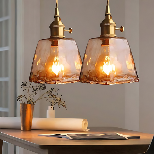 Zwei hängende, bernsteinfarbene Glaspendelleuchten über einem Tisch, warmes Licht, modernes Design.
