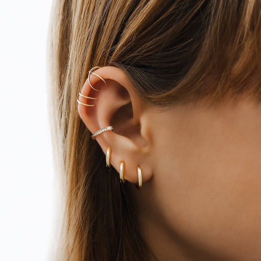 Ohrringe aus Gold an Ohr, modischer Schmuck, elegantes Design, Damenaccessoire.