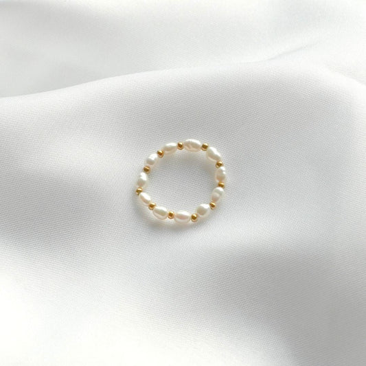 Echter Perlenring auf weißem Stoff, eleganter Schmuck, zeitloses Design, Damenaccessoire.