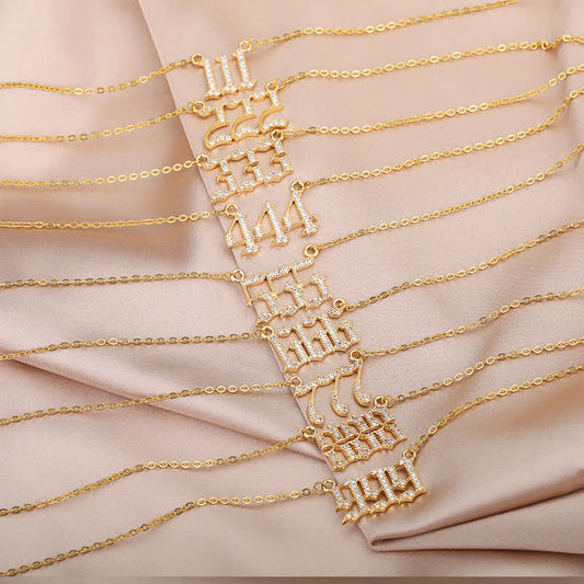 Goldene Armbänder mit Zahlenanhängern auf beigem Stoff, Schmuck, modisch, elegant.