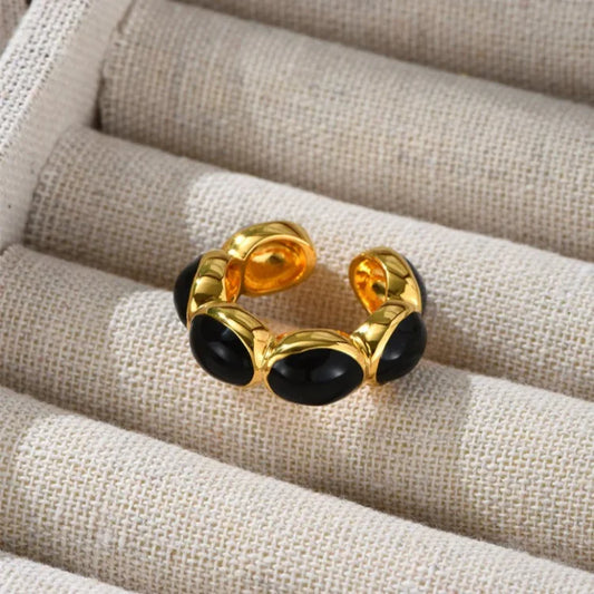 Goldener verstellbarer Ring mit schwarzen Steinen auf beigem Stoff, elegantes Schmuckdesign.