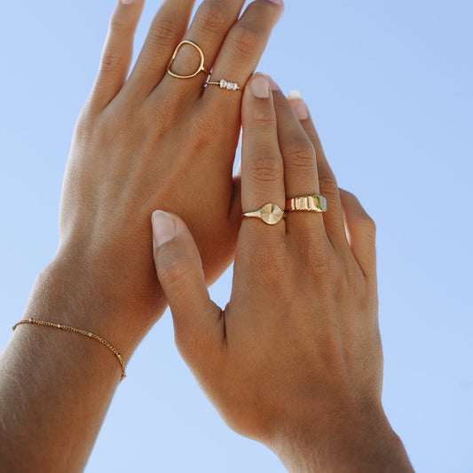 Zarte goldene Armbänder und Ringe auf Händen vor blauem Himmel.