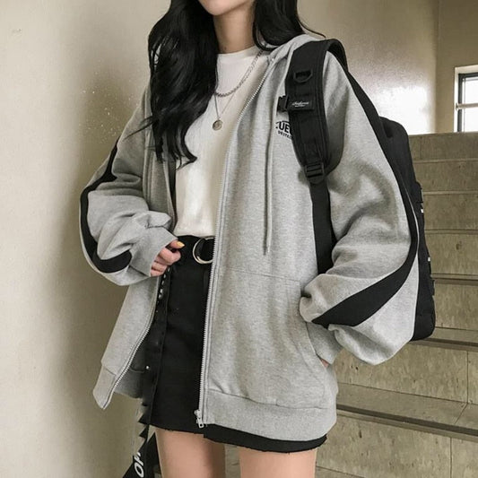 Frau in grauem Hoodie mit schwarzem Rucksack und Rock, lässige Mode, Streetwear-Look.