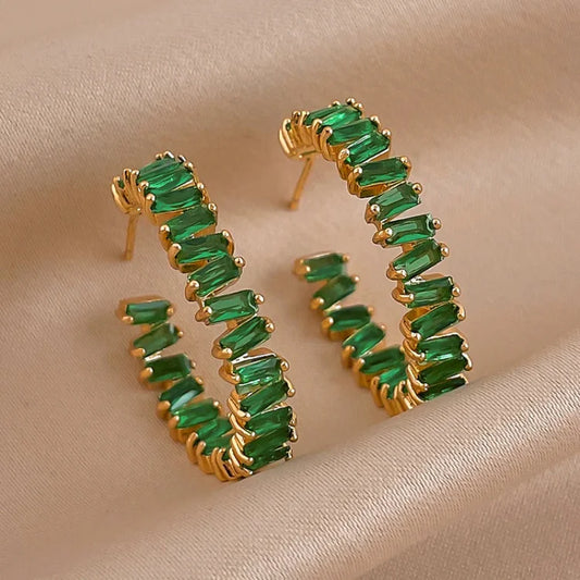 Goldene Creolen mit grünen Edelsteinen auf beigem Stoff, eleganter Schmuck, modische Ohrringe.