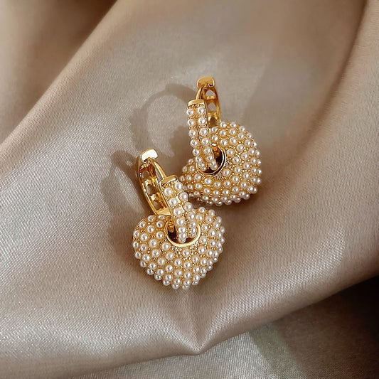 Goldene Herz-Ohrringe mit Perlen auf beigem Stoff, eleganter Schmuck, modische Accessoires.