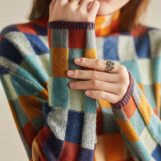 Frau trägt karierten Pullover in bunten Farben, zeigt silbernen Ring, Herbstmode, Nahaufnahme.
