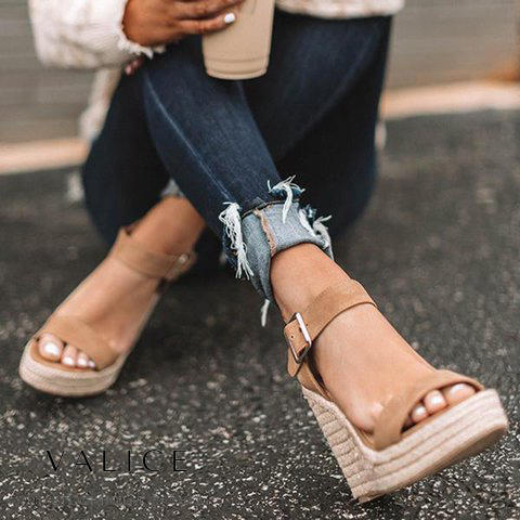 Frau trägt beige Keilsandalen aus Wildleder mit Schnalle, zerrissene Jeans, modisch, lässig.