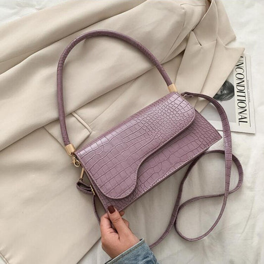 Lila Krokodilleder-Handtasche auf beigem Mantel, modisches Accessoire für Damen.