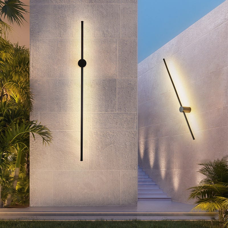 Eine senkrechte und eine schräg gedrehte schwarze Stab-Wandlampe an hellen Steinwänden im Garten mit Palmen und Treppe. 5
