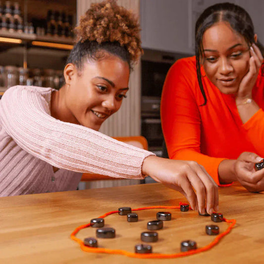 Zwei Frauen spielen mit magnetischem Schachspiel auf Holztisch, lächelnd und konzentriert.