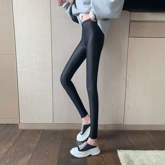 Damen schwarze Leggings, glänzend, figurbetont, mit grauem Hoodie und weißen Sneakers.