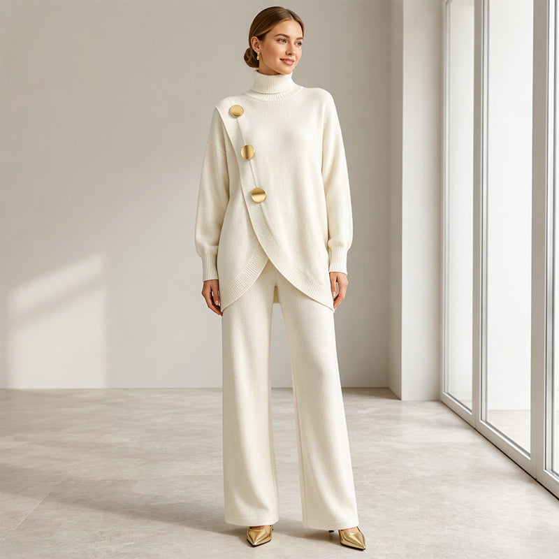 Lächelndes Model in cremeweißem Strickset, Arme locker herabhängend, goldene Pumps, frontale Ganzkörperansicht im hellen Raum. 7