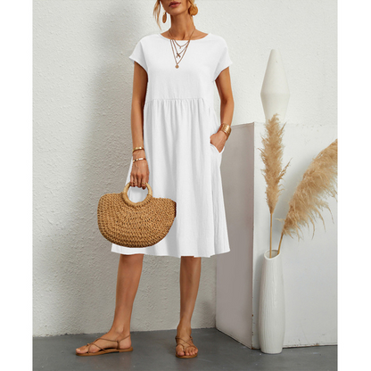 Frau in weißem Baumwoll-Leinen-Kleid, Boho-Stil, mit Strohtasche und Sandalen.
