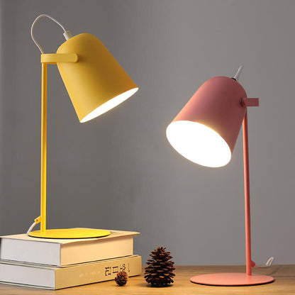 Zwei eingeschaltete Tischlampen im Vergleich, eine gelbe auf Büchern und eine rosafarbene auf dem Holztisch, daneben ein Tannenzapfen. 5
