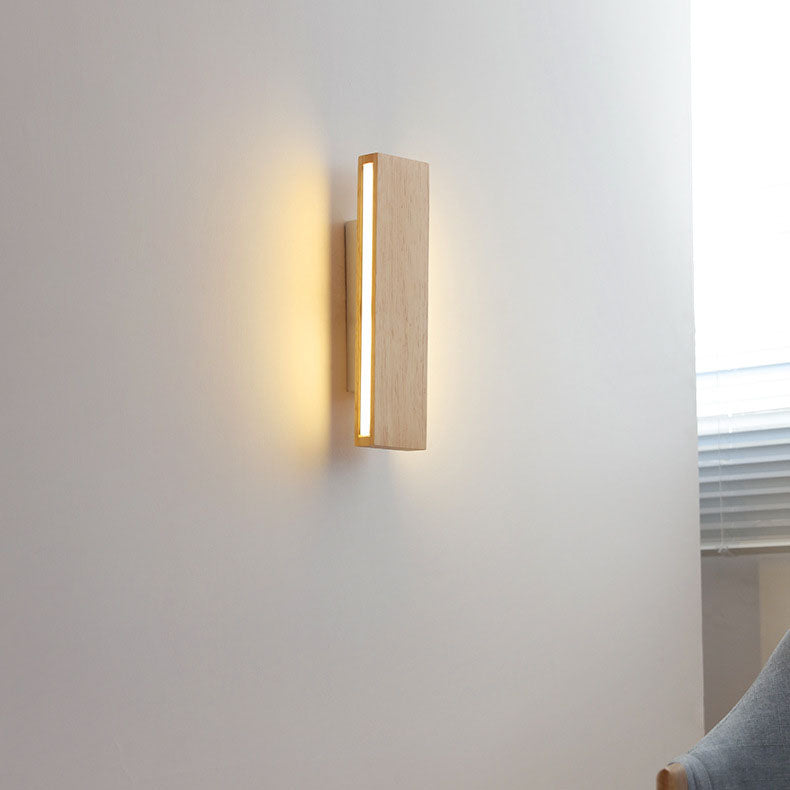 Senkrecht montierte leuchtende Holzlampe an einer Wand neben Fenster mit Jalousie und grauem Sessel. 15