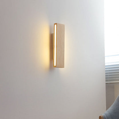 Senkrecht montierte leuchtende Holzlampe an einer Wand neben Fenster mit Jalousie und grauem Sessel. 15