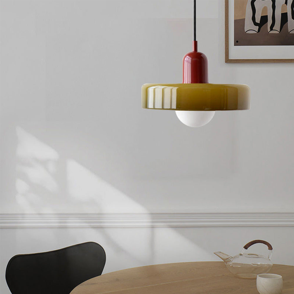 Moderne Hängelampe aus Glas in Rot und Gelb über Holztisch, minimalistisches Design.