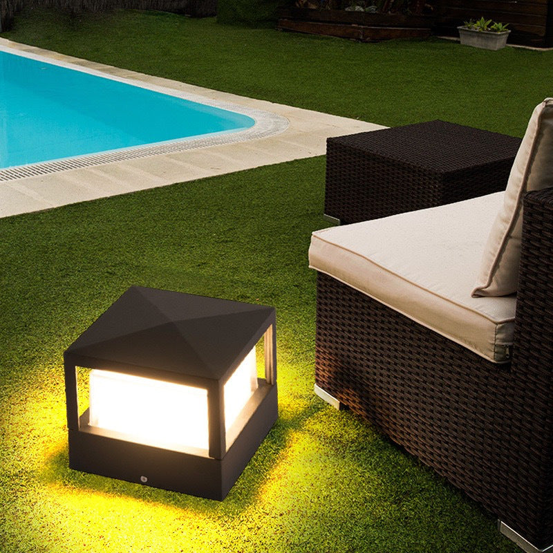 Quadratische Leuchte mit pyramidenförmigem Dach im Rasen neben Rattansofa und Pool, die das Gras gelblich anstrahlt. 4